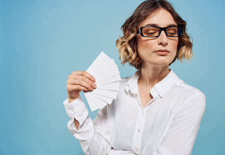 A woman in glasses with a bundle of business cards in her hands on a blue background