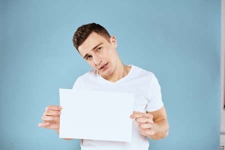 a man in a white t-shirt holds a sheet of paper copy spaceの写真素材