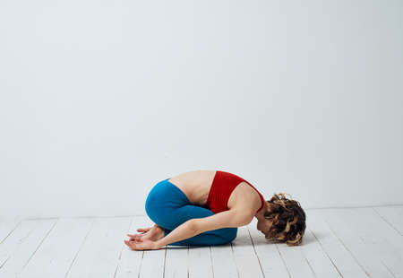 A slender woman is engaged in yoga for beginners on a light background in full growth