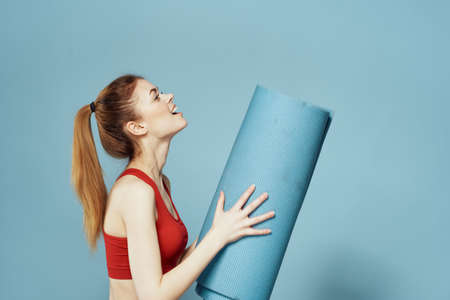 athletic woman with fitness mat exercise slim figure red t-shirt blue background