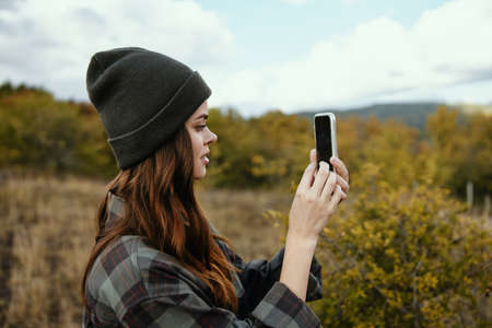 Woman with mobile phone in the autumn forest and mountains in the backgroundの写真素材