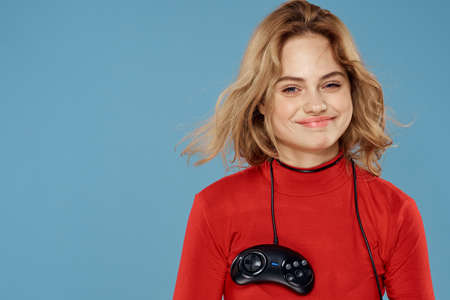 Pretty woman gamepad in hands playing games entertainment consoles to lifestyle blue background red jacketの写真素材