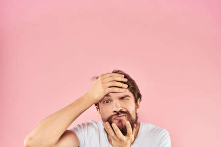 Bearded man in white t-shirt gesturing with hands facial expression close up pink background