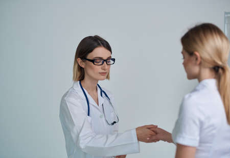 woman doctor in a medical gown shakes hands with a patient in a white t-shirt on a light backgroundの写真素材