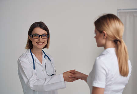woman doctor in a medical gown shakes hands with a patient in a white t-shirt on a light backgroundの写真素材