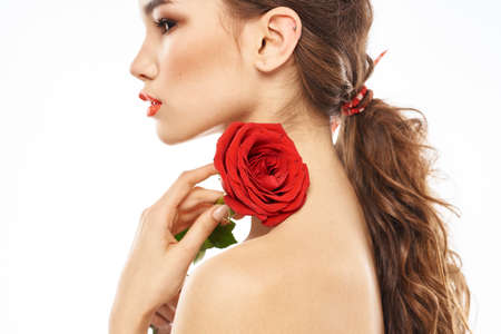 Beautiful woman with red rose near face makeup naked shoulders portraitの写真素材