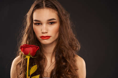 woman with a red rose on a dark background long hair makeup red lipsの写真素材