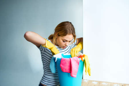 Woman with a bucket of cleaning supplies near the window taking care of the houseの写真素材