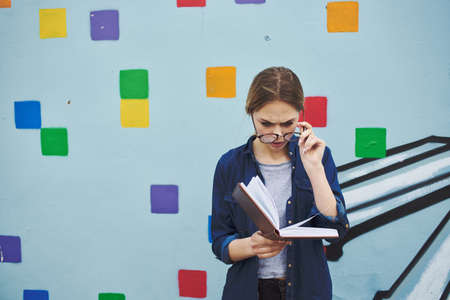 A woman with a notebook in her hand near a multicolored graffiti on the street