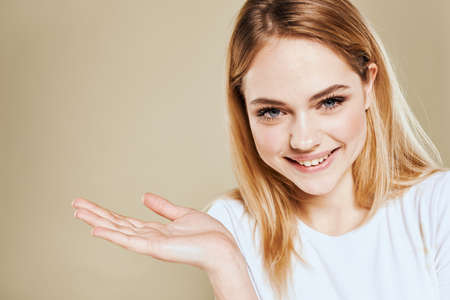 Cheerful woman in a white T-shirt gestures with her hands emotions beige backgroundの写真素材