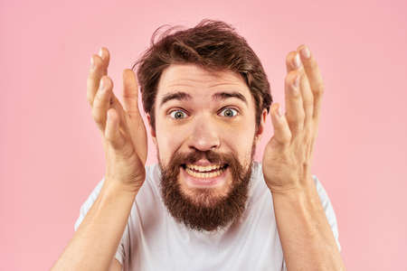 Bearded man in white t-shirt gesturing with hands facial expression close up pink backgroundの写真素材