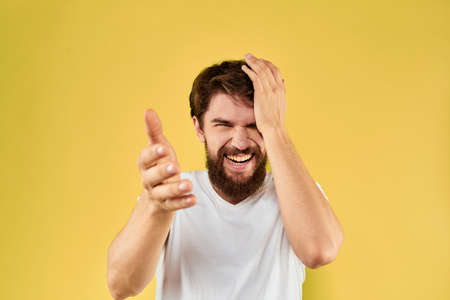 Bearded man emotions fun gesture with hands white t-shirt close-up yellow background