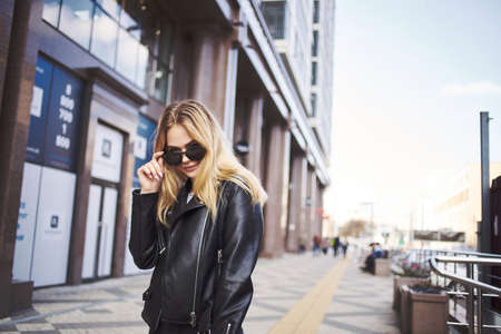 Fashionable woman in a leather jacket and sunglasses near the building