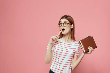 female student with notepads on pink background gesturing with her hands glasses on her face striped...