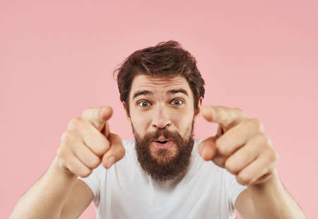A man with a beard gestures with his hands on a pink background cropped view of a white t-shirt