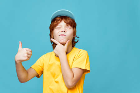 Red-haired boy holding his chin showing thumb up cropped view