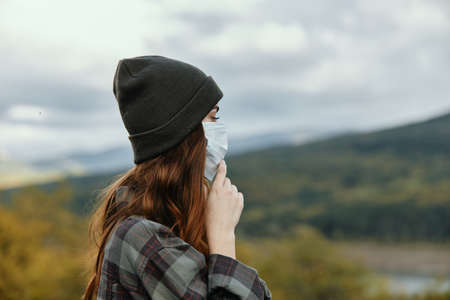 Woman with hat and medical mask checkered shirt mountains nature autumnの写真素材
