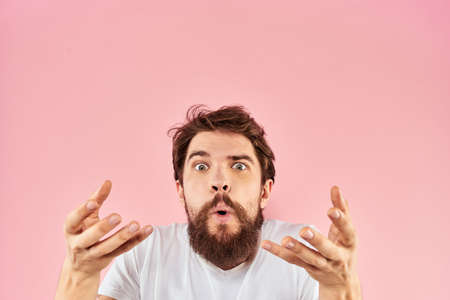 Bearded man in white t-shirt gesturing with hands facial expression close up pink background