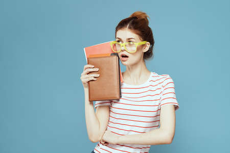 Female student with books in hands on a blue background and yellow glasses model hairstyle cropped...