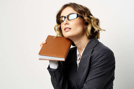 Woman at work with book in hand light background classic suit glasses headの写真素材