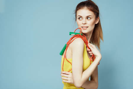 Sportive woman holding a skipping rope yellow tank top exercise gymnastics blue background