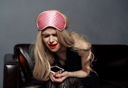 Drunk blonde woman in sleep mask with mobile phone photography model