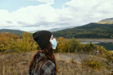 Woman in warm caps in the autumn forest with a medical mask on her faceの写真素材