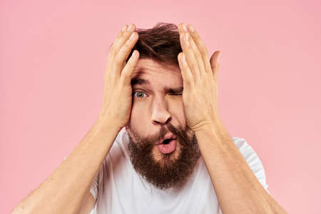 Bearded man in white t-shirt gesturing with hands facial expression close up pink background