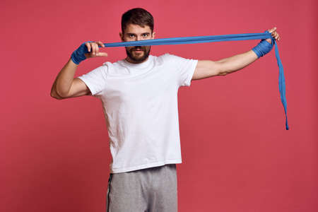 man in white t-shirt ties his hand with a bandage martial arts pink background