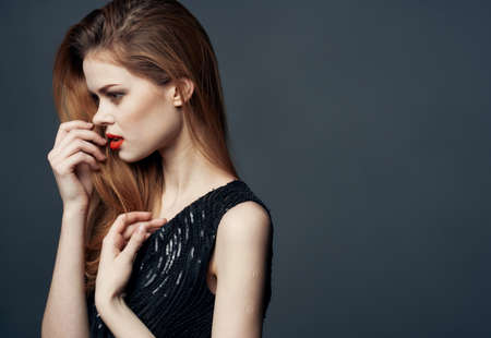 A woman in a black dress with red hair on a gray background gestures with her hands