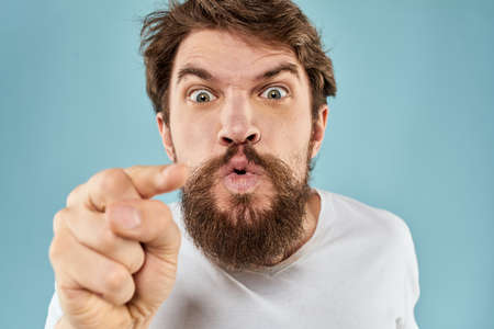 Bearded man in white T-shirt emotions gestures with hands displeased facial expression blue backgroundの写真素材