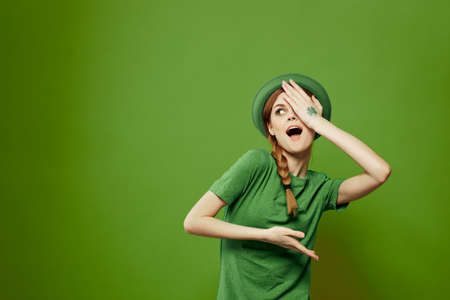 Happy woman with shamrock on St. Patricks Day in green clothes and a hat on her head gesturing with...