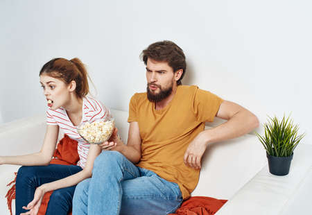 A man and a woman on the couch watching TV with popcorn in a plate