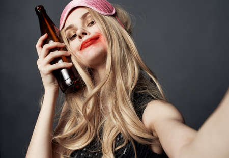 Drunk woman with a bottle of beer on a gray background gestures with her hands and bright makeupの写真素材