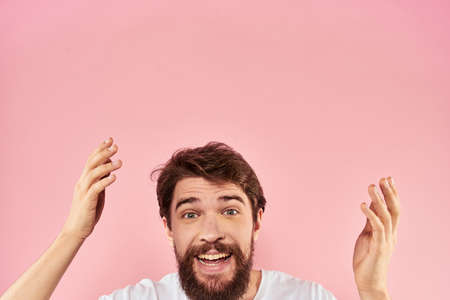 Bearded man in white t-shirt gesturing with hands facial expression close up pink background
