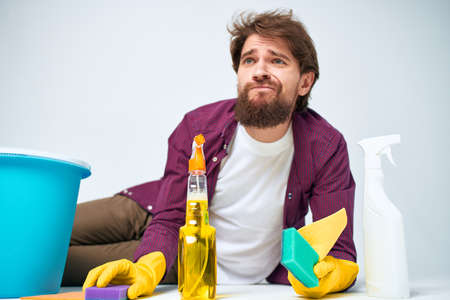 A man lies on the floor with a bucket of detergents providing services light backgroundの写真素材