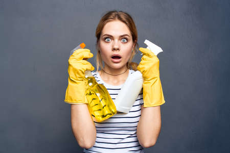 Emotional cleaning lady wearing yellow rubber gloves with detergent gray background
