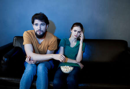 Handsome man and young woman on sofa indoors watching TV in the evening