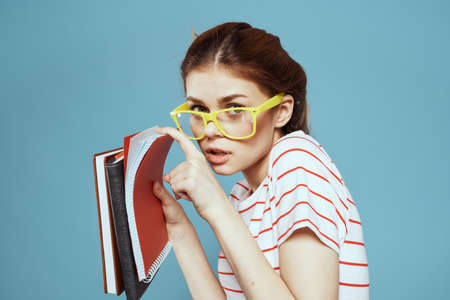 Beautiful female student with notepads and in yellow glasses on a blue background education science instituteの写真素材