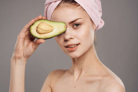Woman with bared shoulders avocado in hands cropped view over gray backgroundの写真素材