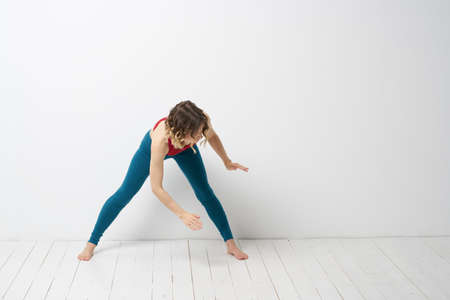sports woman in a bright room doing yoga in full growth blue leggings and a red tank top
