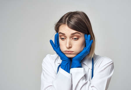 A nurse in a medical gown and blue gloves gestures with a stethoscope around her neck