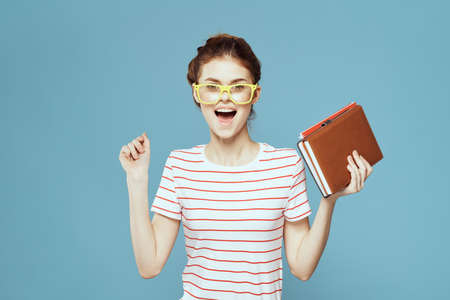 Female student with books in hands on a blue background and yellow glasses model hairstyle cropped...