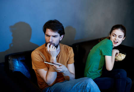 A man with a mobile phone and a pretty woman watching TV indoors in the eveningの写真素材