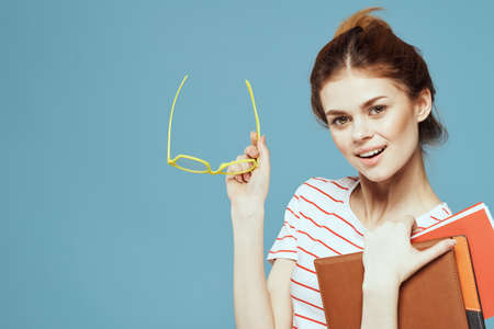 Beautiful female student with notepads and in yellow glasses on a blue backgroundの写真素材