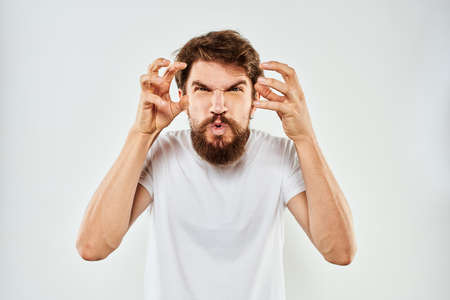 Emotional bearded man in a white t-shirt gestures with his hands light backgroundの写真素材
