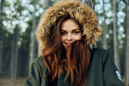 woman with a hood on her head in a jacket coolness on the background of the forest travel