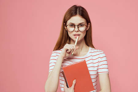 female student with notepads on pink background gesturing with her hands glasses on her face striped...