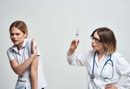 A woman holds a syringe in her hand and a female patient in a white t-shirt is frightened modelの写真素材