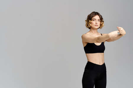 A slender woman in black leggings on a gray background gestures with her hands gymnastics sports